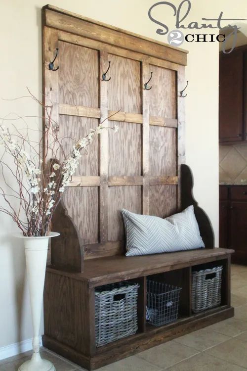 a wooden bench with baskets on it in front of a wall mounted coat rack and shelf