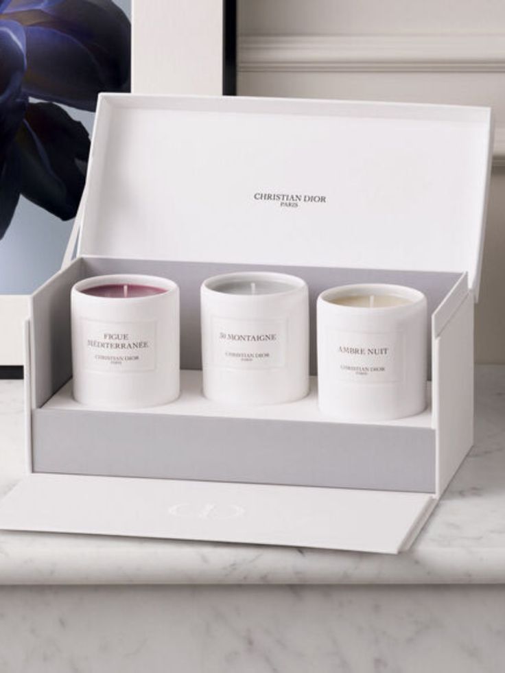 three candles in a white box sitting on a marble counter next to a framed photograph