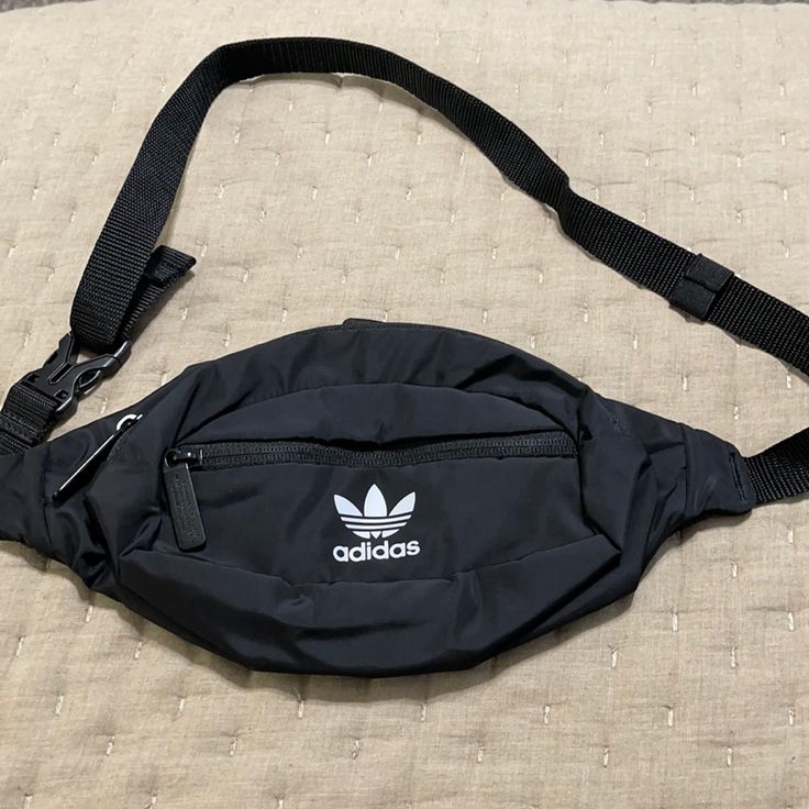 an adidas fanny bag laying on top of a bed next to a black strap