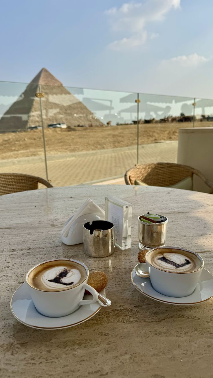 two cups and saucers sitting on top of a table near the pyramids in egypt