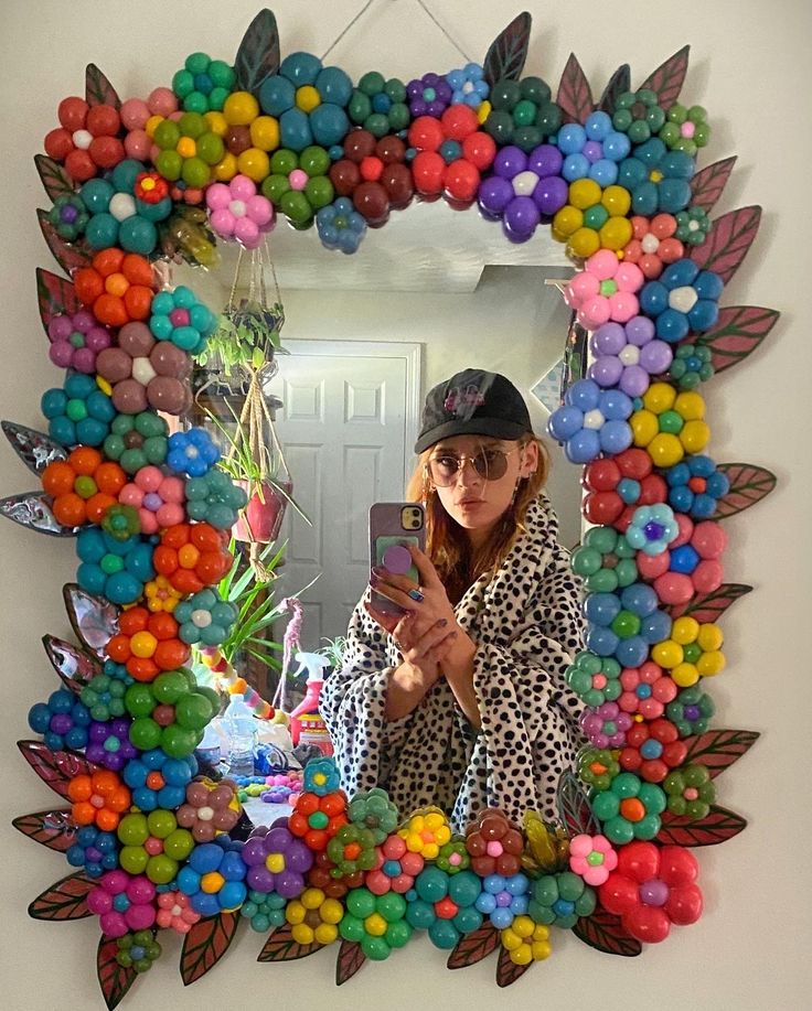 a woman taking a selfie in front of a colorful wreath made out of balloons