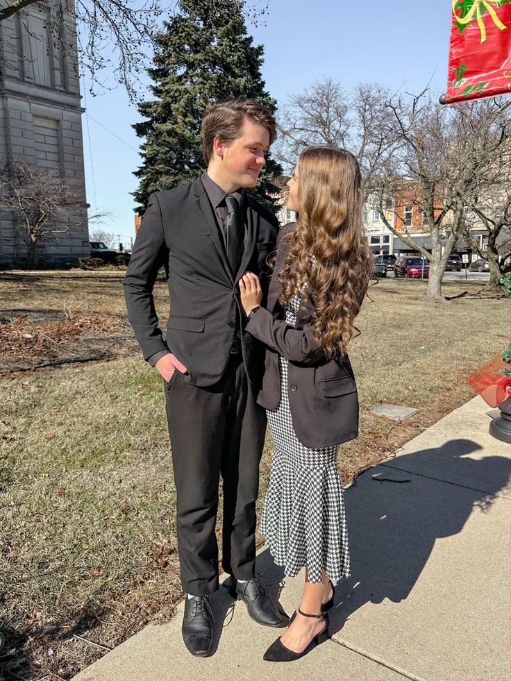 a man in a suit and tie standing next to a woman on a sidewalk near a christmas tree