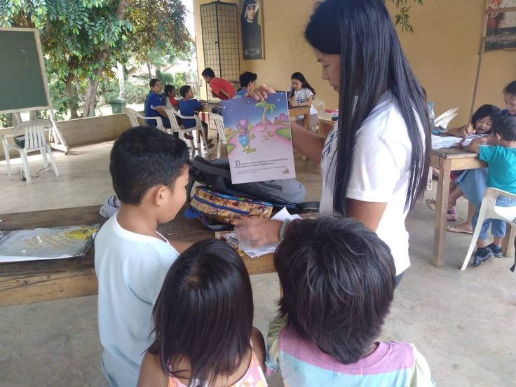 a woman standing in front of children at a table with paper and scissors on it