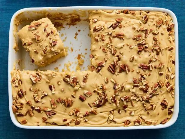 a white dish filled with cake covered in pecans and caramel topping on top of a blue table