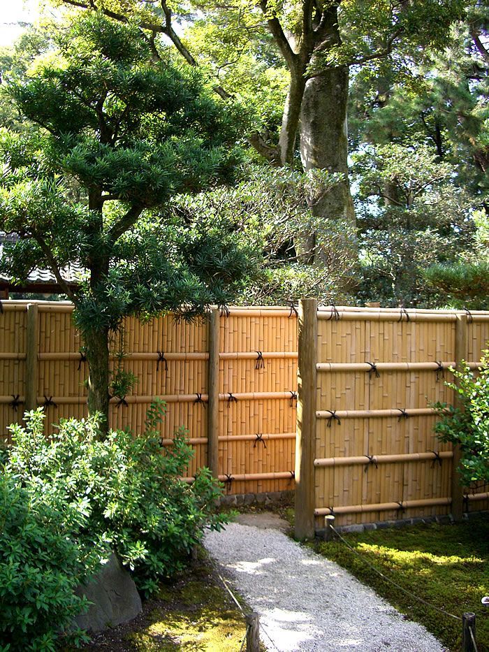 a wooden fence in the middle of a garden with trees and rocks on the ground