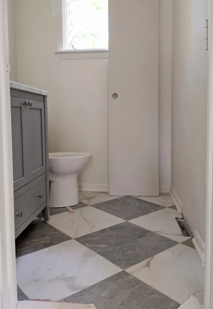 a white toilet sitting in a bathroom next to a sink under a window on top of a checkered floor