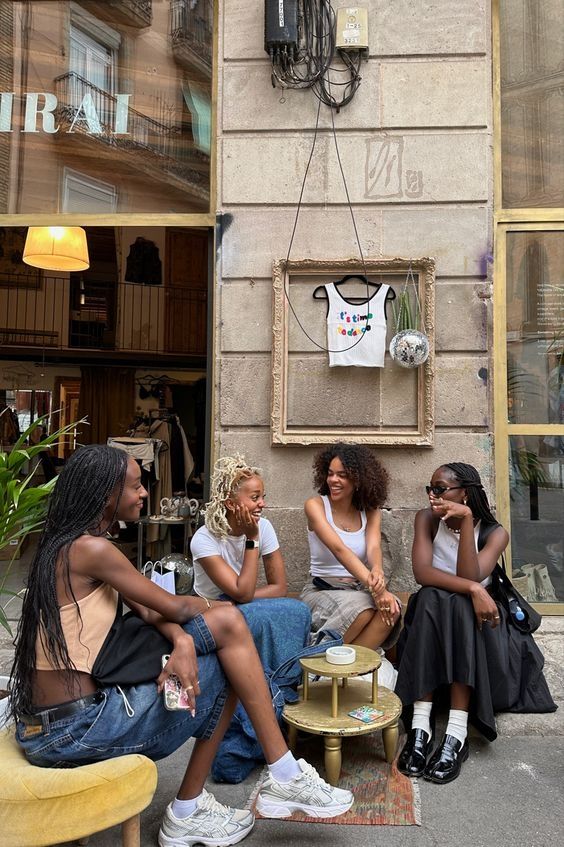 three women sitting on the sidewalk talking to each other in front of a store window