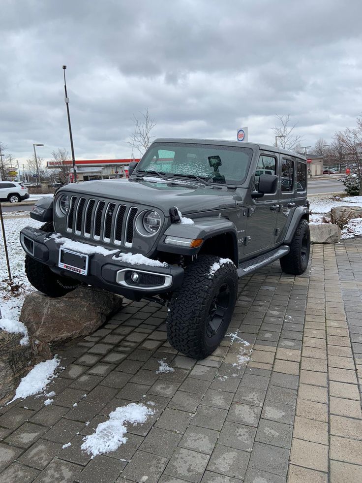 a gray jeep parked on the side of a road next to a pile of snow