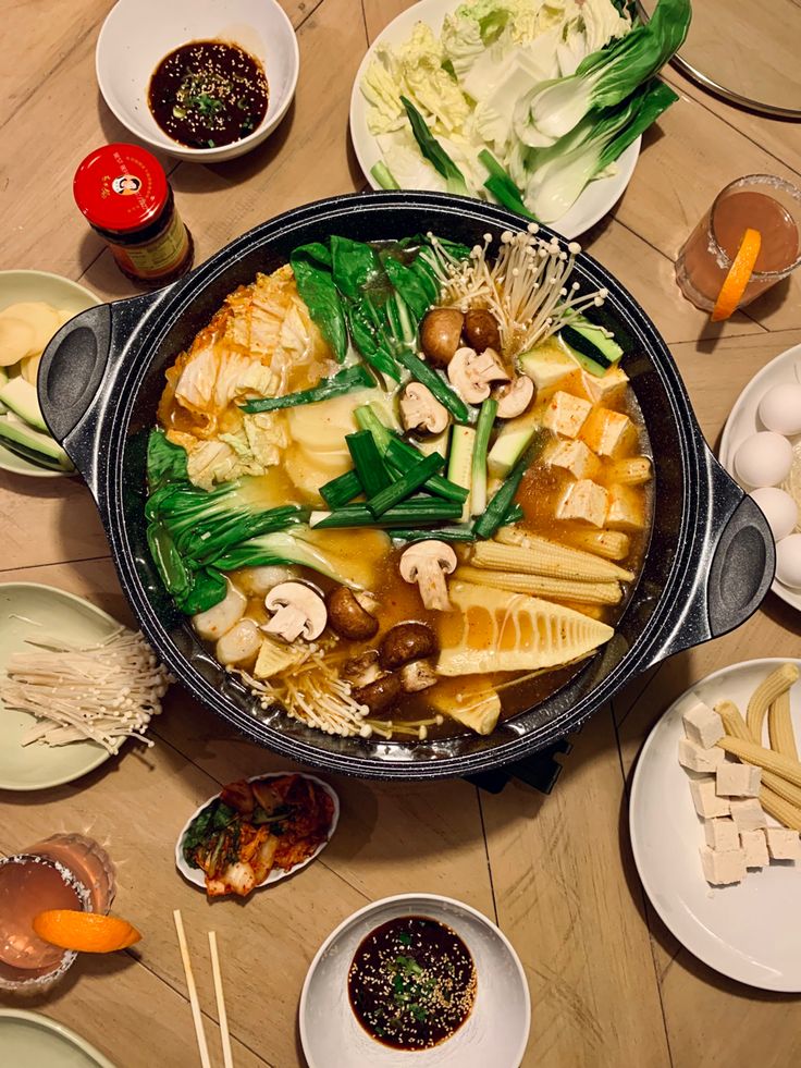 a large pot filled with lots of food on top of a wooden table next to plates and bowls