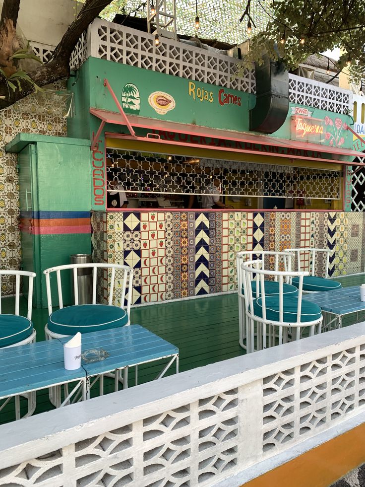 tables and chairs are set up outside in front of a restaurant with colorful tiles on the walls