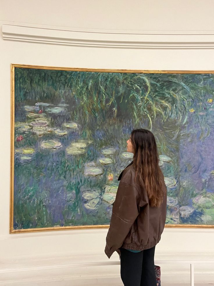 a woman standing in front of a painting with water lillies on it's wall