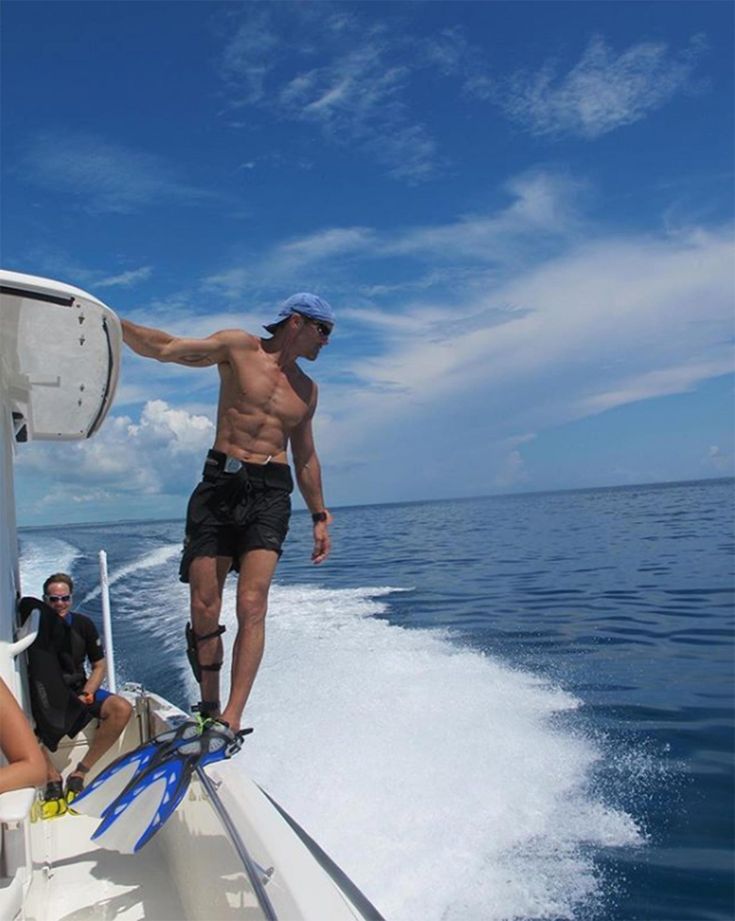 a man standing on the back of a boat while two people ride in the water