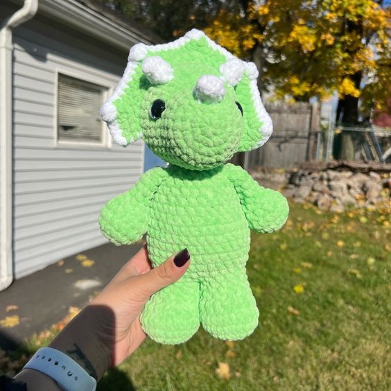 a hand holding a green teddy bear in front of a house