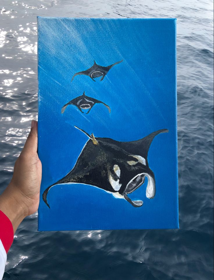 a painting of a manta ray being held up by a person's hand