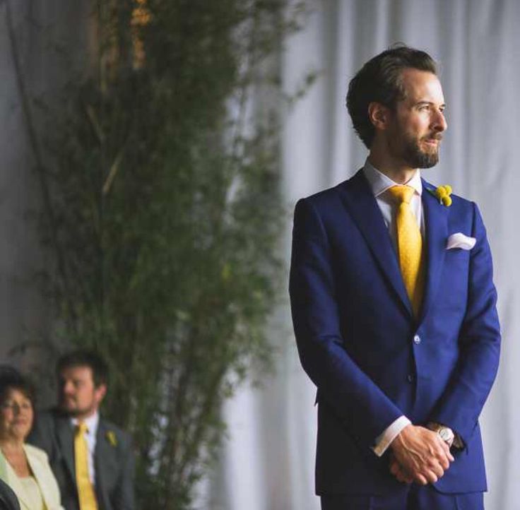 a man wearing a blue suit and yellow tie standing in front of a group of people