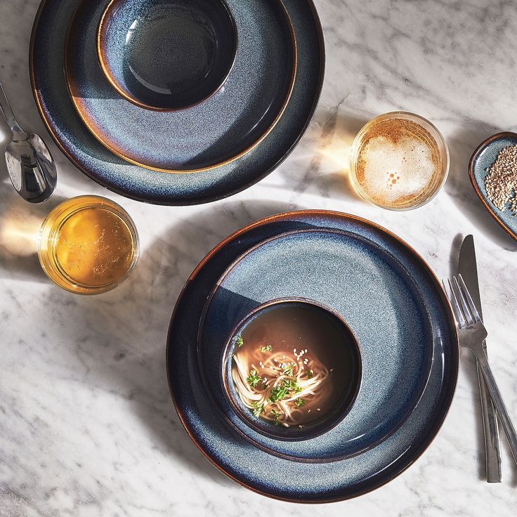 two plates with soup and spoons on a marble table top next to silverware