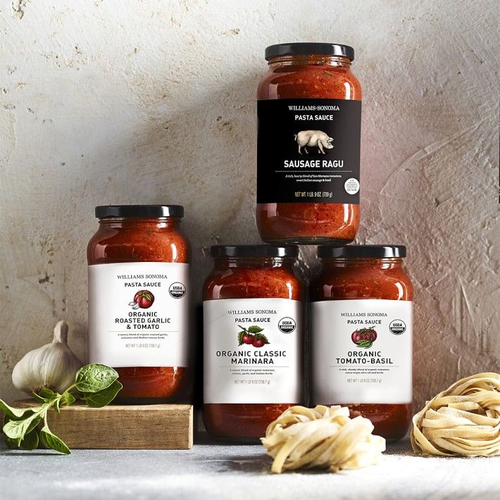 four jars of pasta sauce sitting on top of a table next to garlic and basil