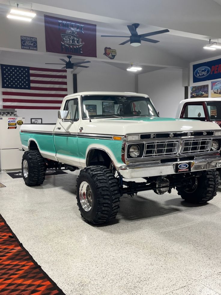 two trucks are parked in a garage with an american flag on the wall behind them