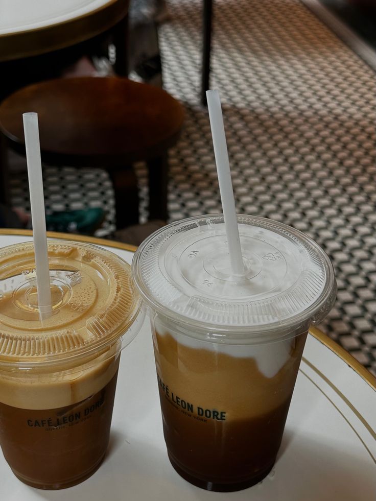 two iced coffees sitting on top of a white plate with straws in them