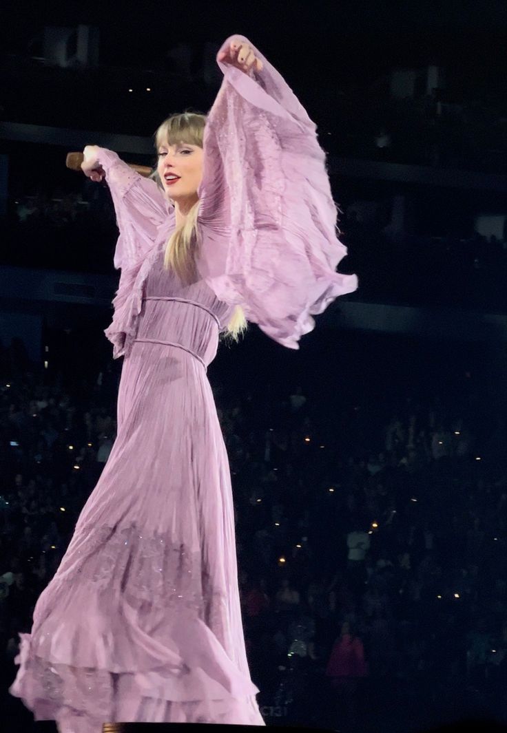 a woman in a long purple dress is performing on stage with her arms spread out