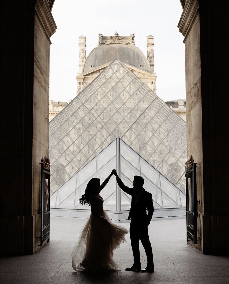 a man and woman standing in front of a building with a glass pyramid behind them