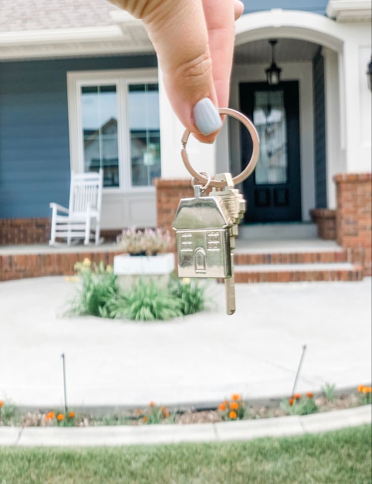 a hand holding a house key in front of a house