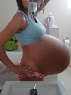 a pregnant woman taking a selfie in the bathroom with her cell phone and camera