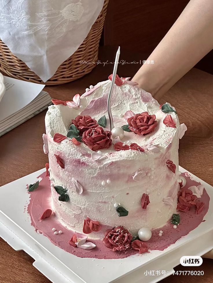 a person cutting into a white cake with pink frosting and roses on it,