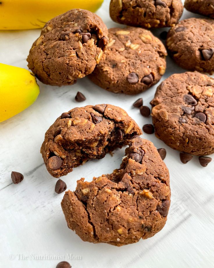 chocolate chip cookies and bananas are on a white surface with one cookie broken in half