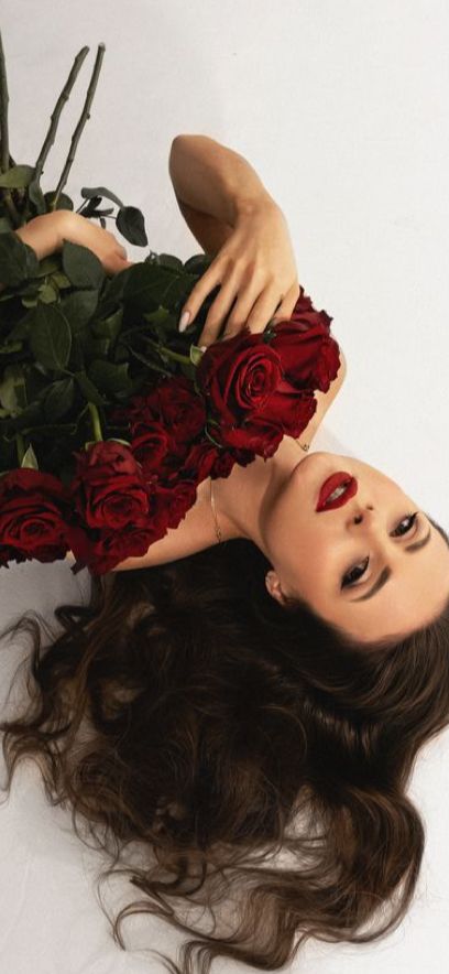 a woman laying on the ground with roses in her hair and hands over her head