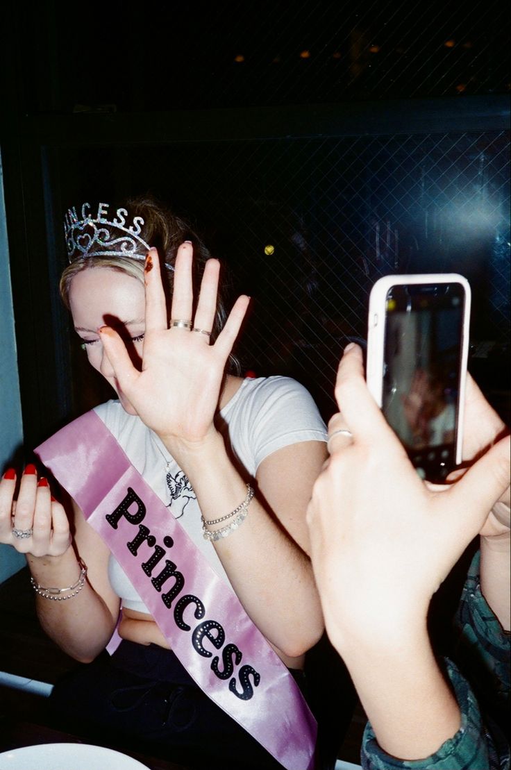 two women taking pictures with their cell phones while one holds her hand up in the air