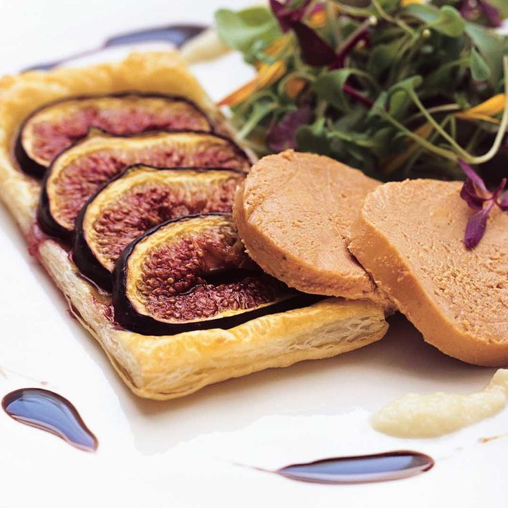 figs and bread on a white plate with some greens in the background, including an eggplant