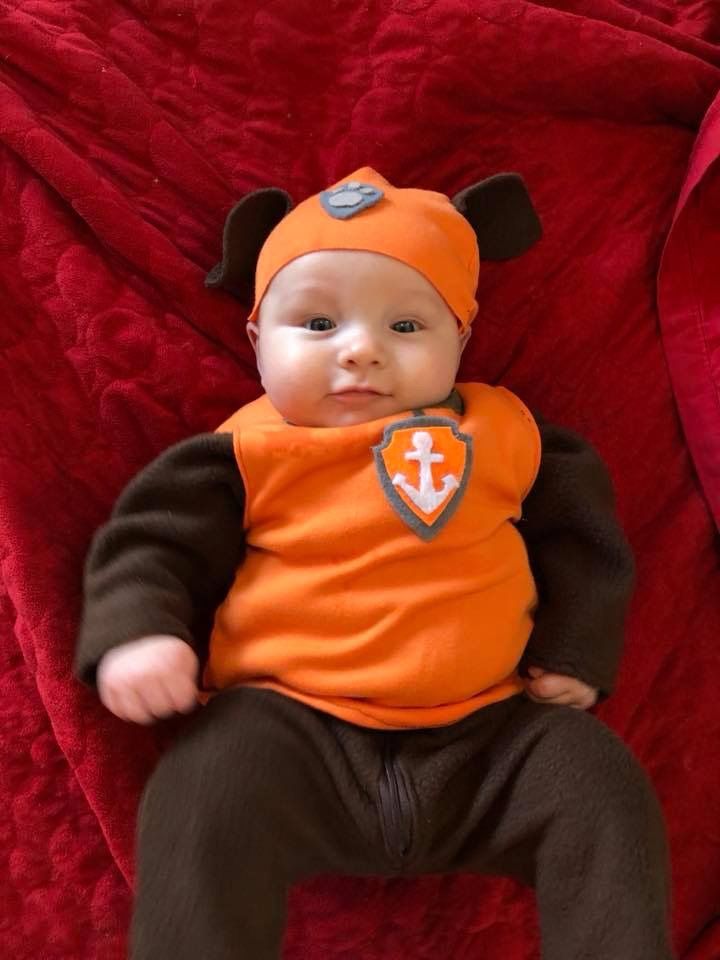 a baby in an orange shirt and black pants is laying on a red bed spread