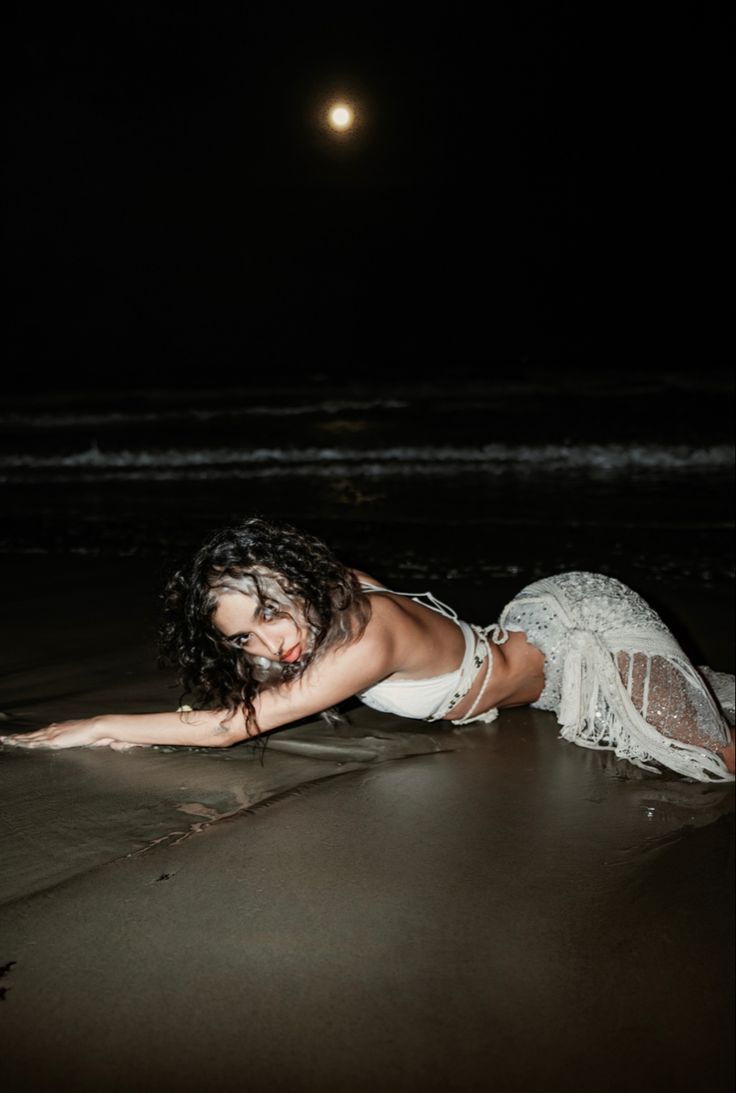 a woman laying on the beach at night with her arms spread out and head down