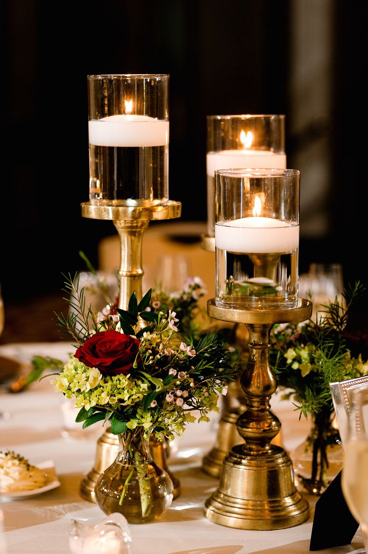 candles are lit on the table with flowers and greenery