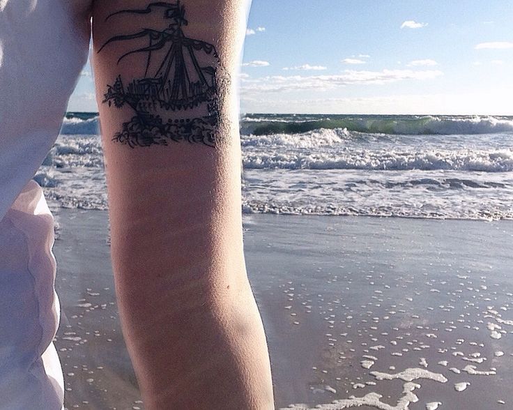 a person with a tattoo on their arm standing in the sand at the beach next to the ocean