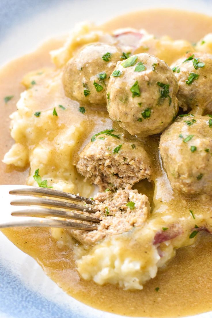 a white plate topped with meatballs covered in gravy and mashed potatoes