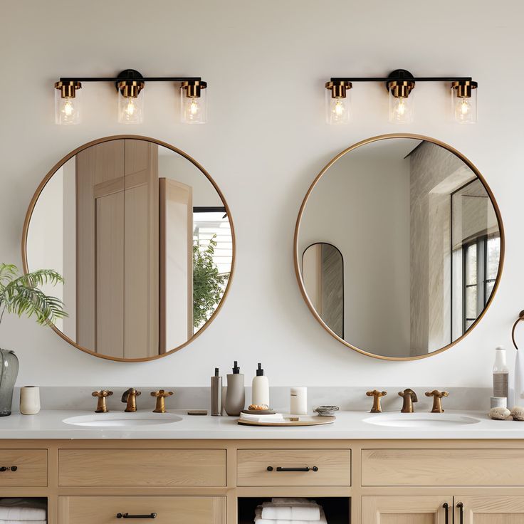 two round mirrors on the wall above double sinks in a white bathroom with wood cabinets