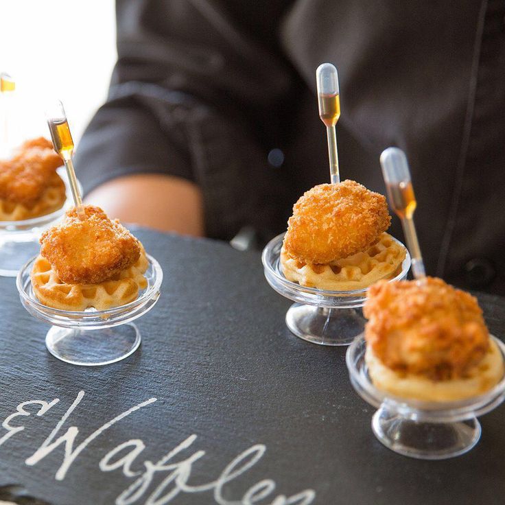 mini waffles are arranged on small clear dishes with forks in them, sitting on a chalk board