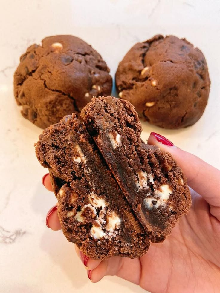 a hand holding a chocolate cookie with white crumbles on it and two other cookies in the background