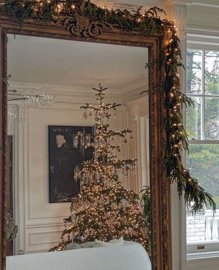 a decorated christmas tree in front of a mirror with lights and garland on the branches