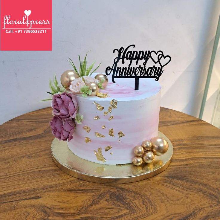 a pink and gold wedding cake on a wooden table with the words happy anniversary written on it