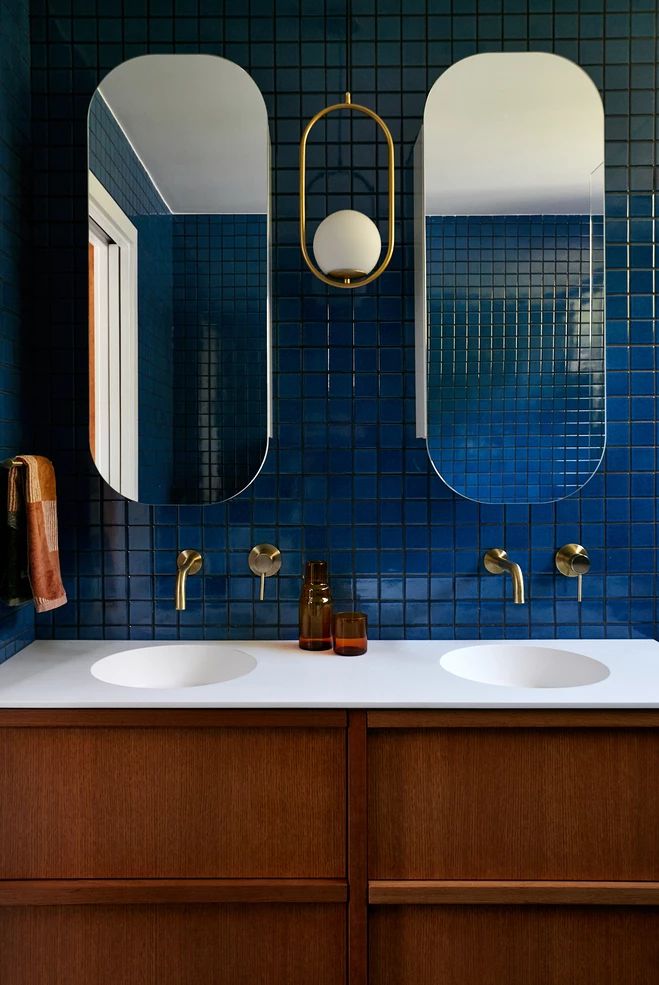 a bathroom with two sinks and three mirrors on the wall in front of blue tiled walls