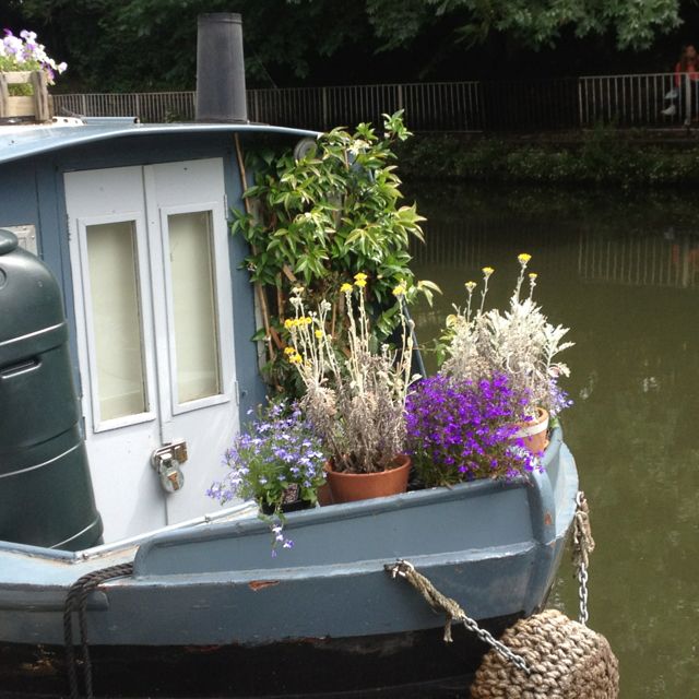 a boat with flowers and plants on the front sits in water next to a dock