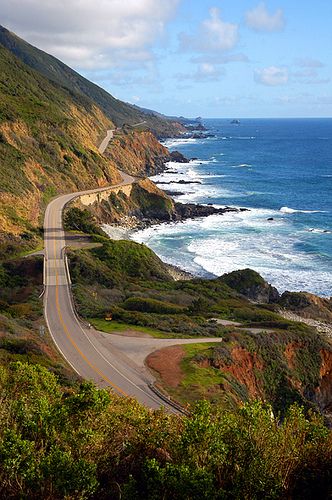 an empty road on the side of a cliff overlooking the ocean and cliffs in the distance