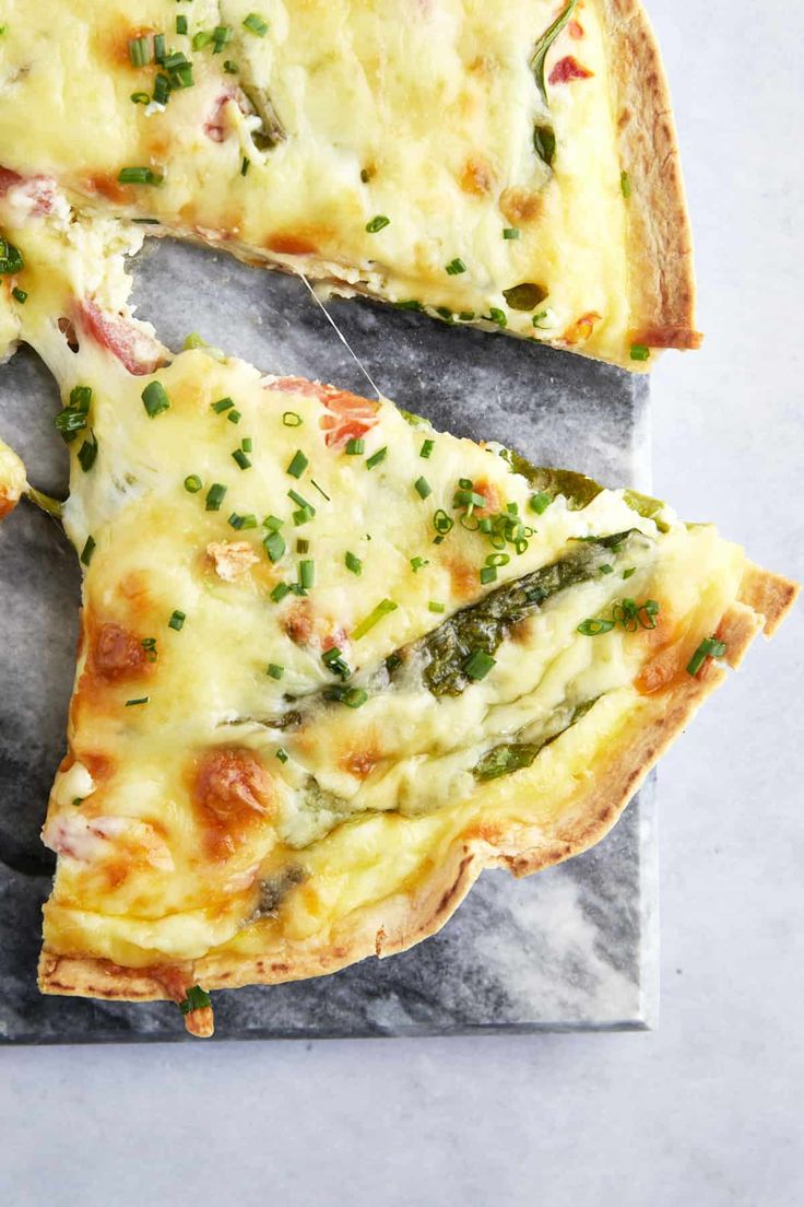 two slices of pizza with cheese and green onions on a marble board next to a fork