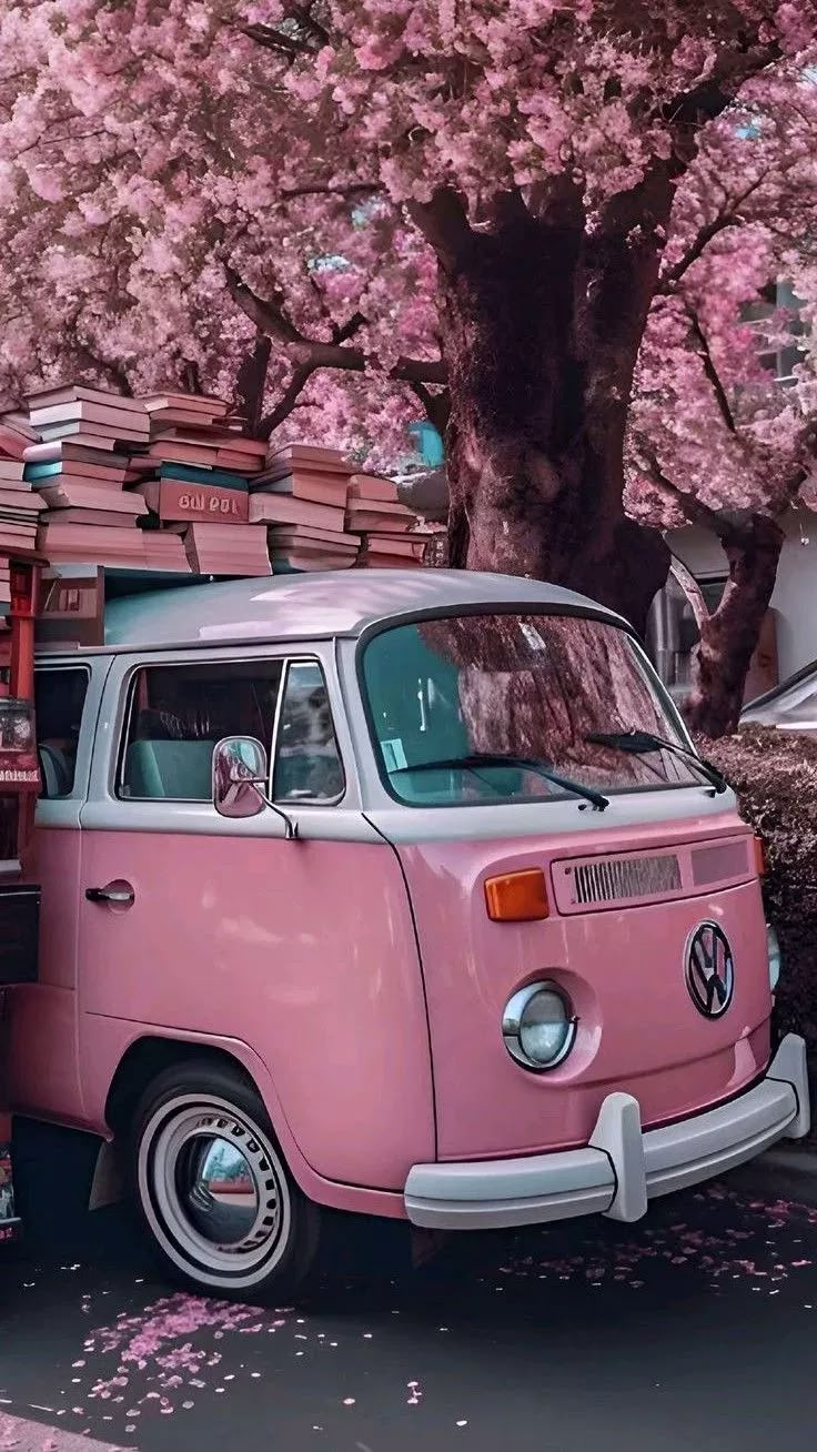 a pink vw bus parked in front of a tree filled with pink blossoming trees