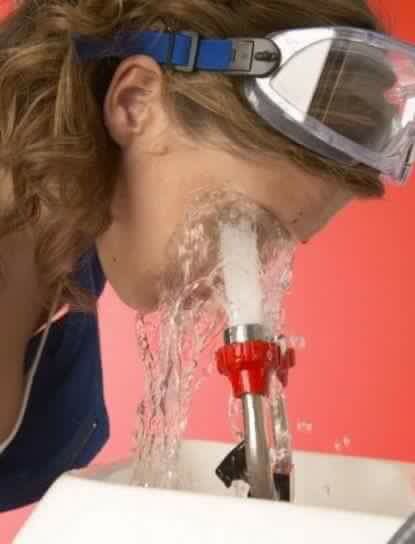 a woman with goggles on drinking water from a faucet in front of her face