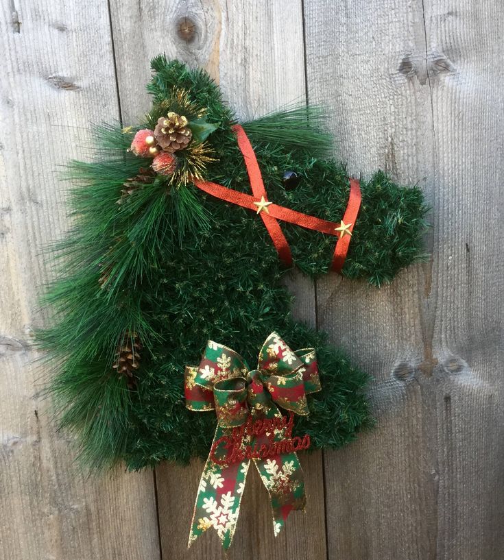 a christmas wreath hanging on the side of a wooden fence with pine cones and bows