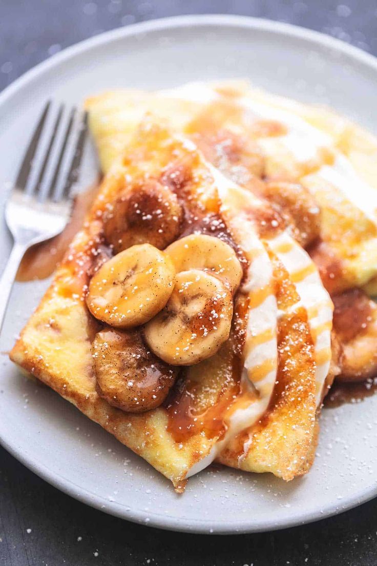 a white plate topped with waffles covered in banana slices and drizzled with powdered sugar